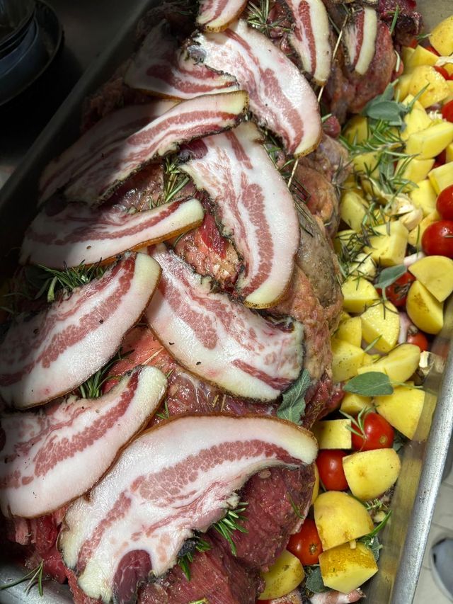 Carne marmorizzata a fette disposta su un piatto con frutta gialla e pomodorini ciliegino