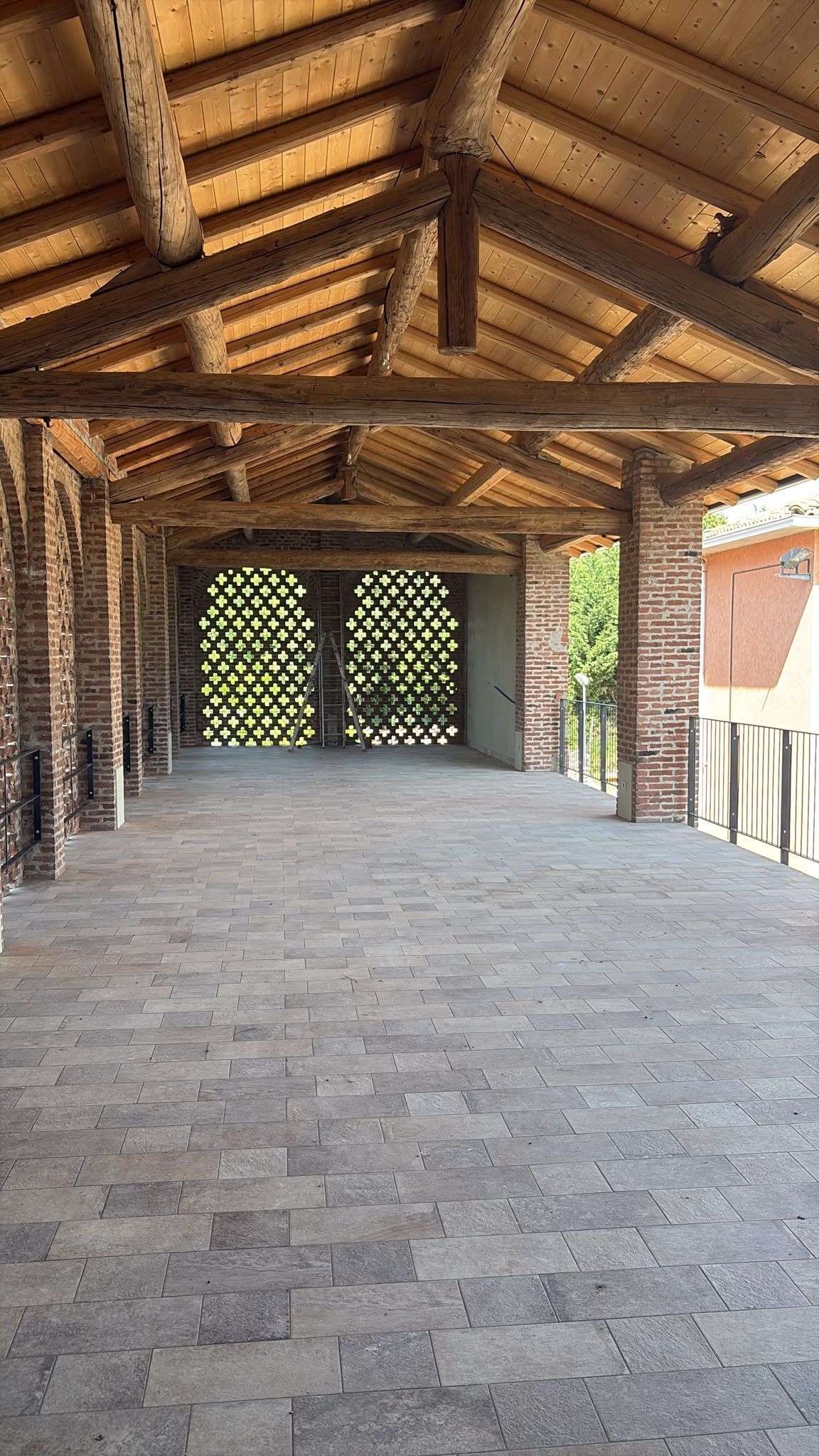 Patio coperto in pietra con tetto in legno e muro a traliccio, che conduce a un cancello chiuso all'esterno.