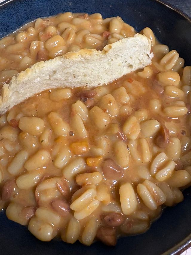 Fagioli bianchi in una ciotola scura, guarniti con una fetta di pane o toast.