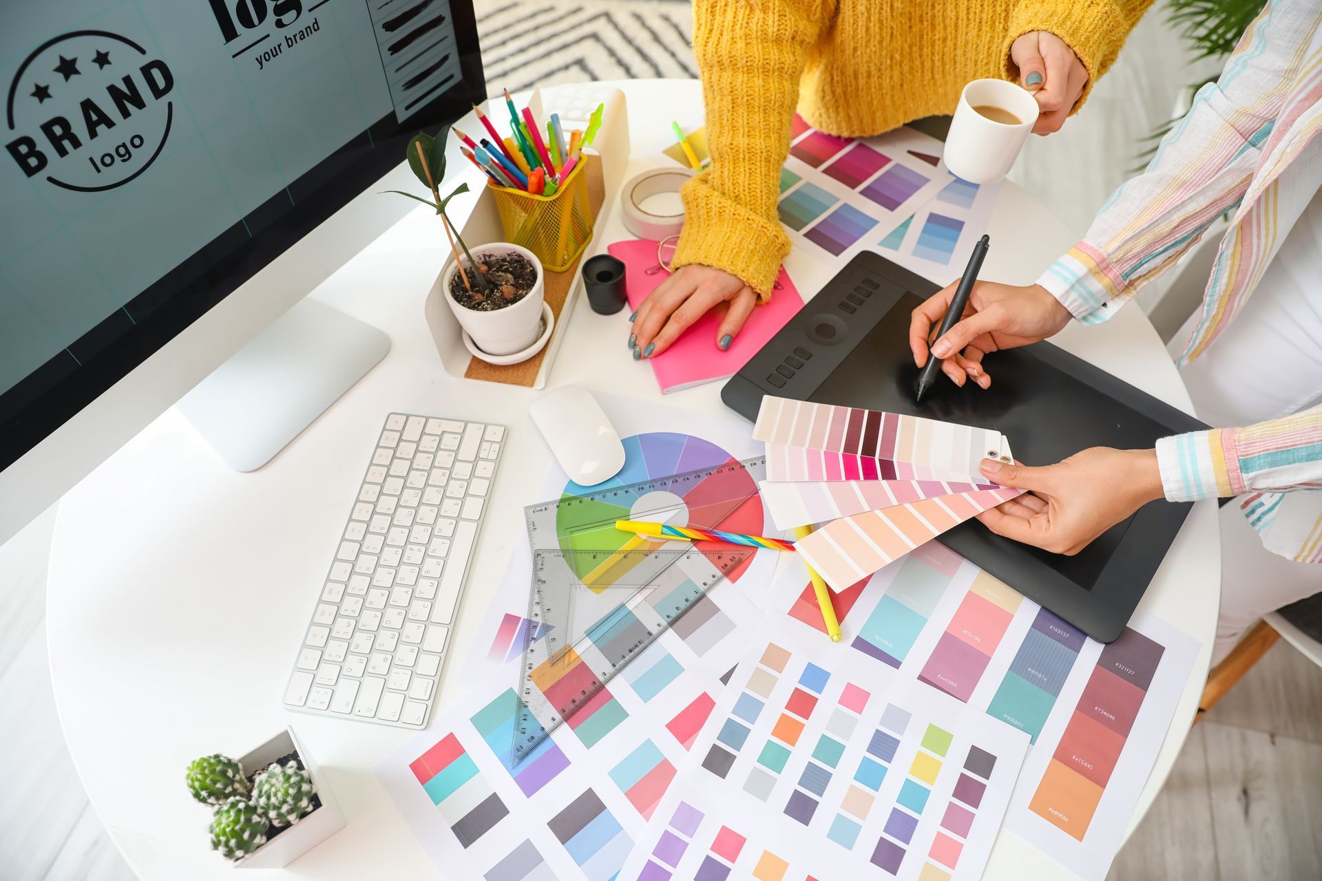 Two people review color swatches and design samples at a bright desk with a computer and stationery.
