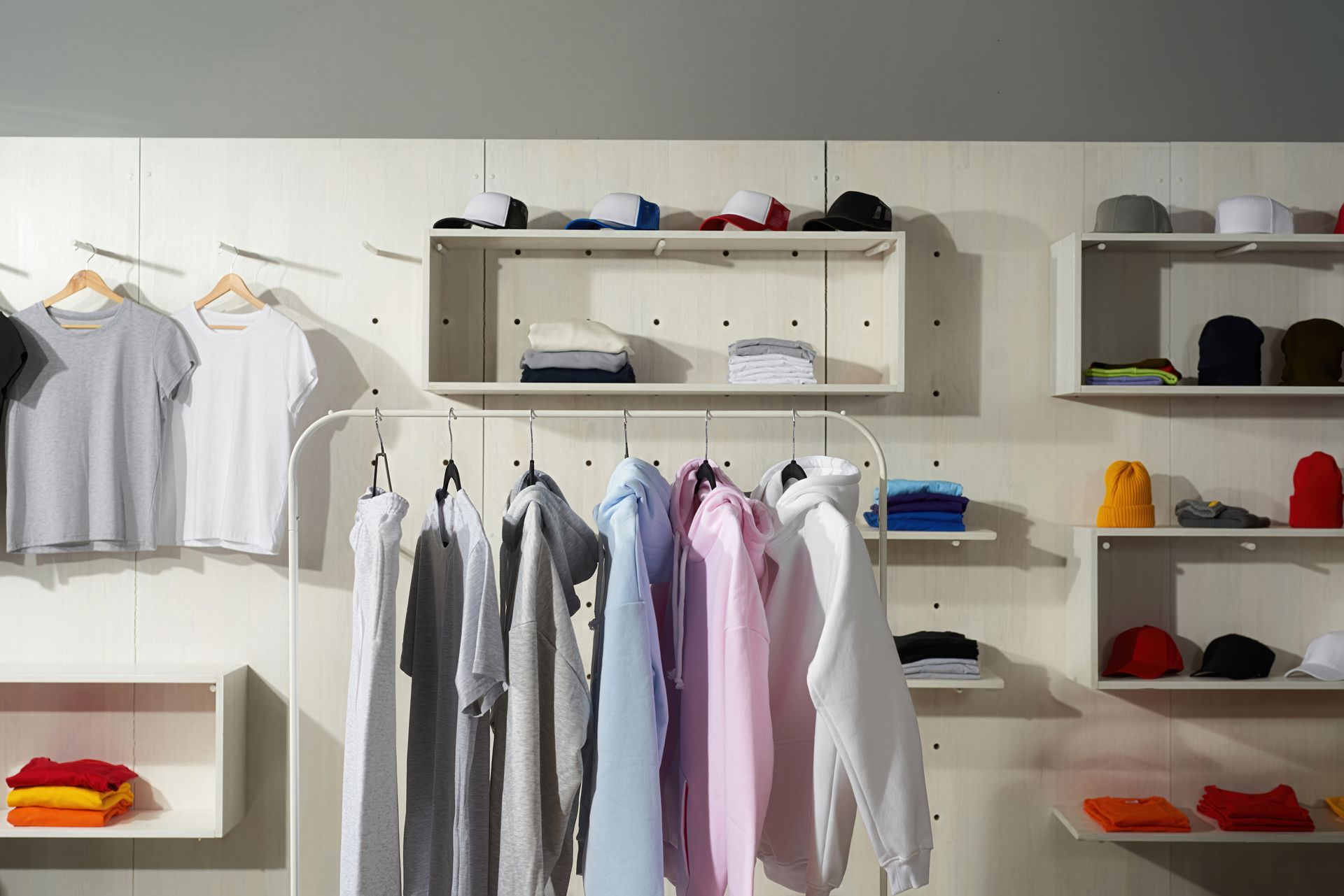 Retail clothing store display with white shirts, hanging tops, and shelves of folded hats and garments