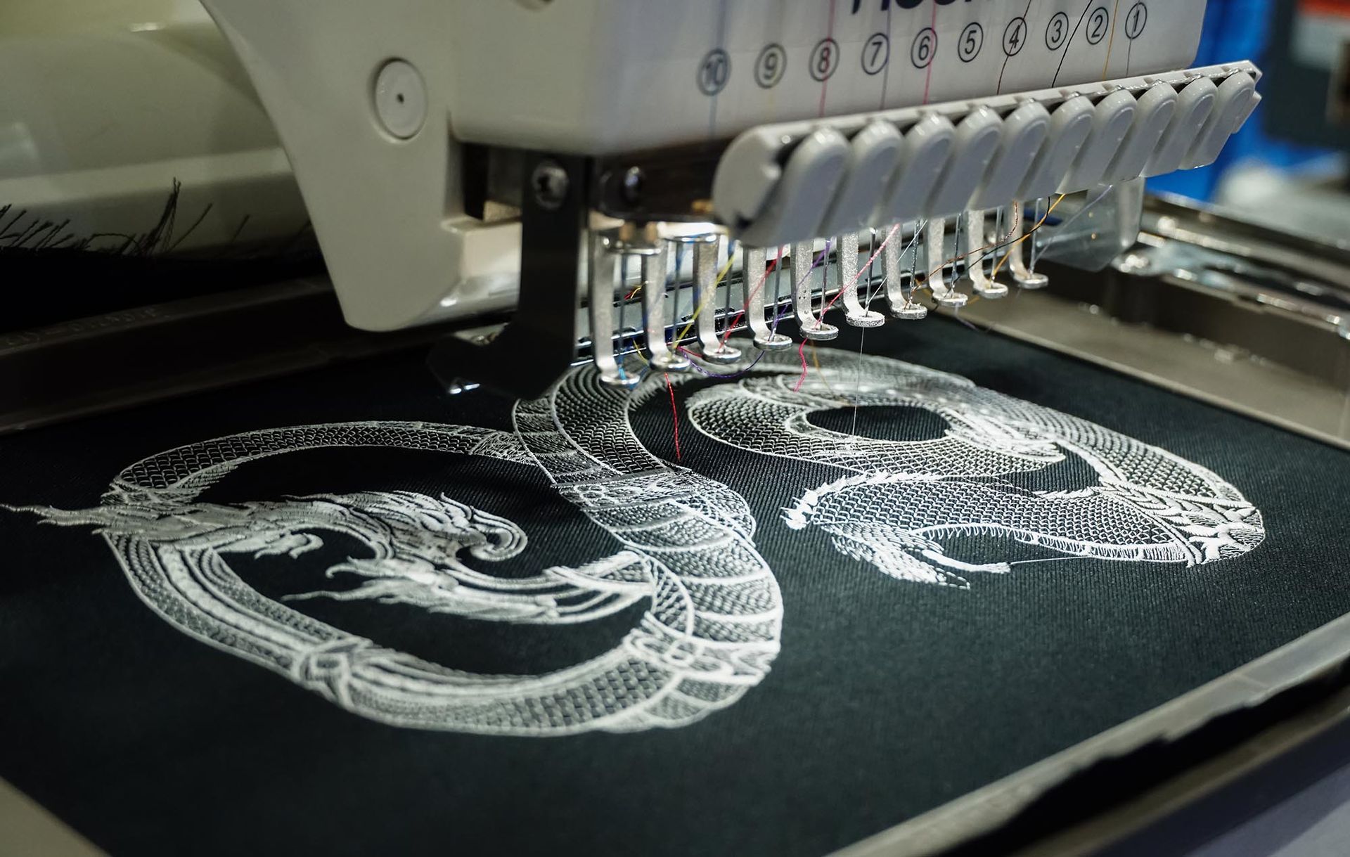 Embroidery machine stitching white thread into a decorative floral design on black fabric