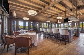 Upscale restaurant dining room with wood beams, chandeliers, white tablecloths, and bar seating