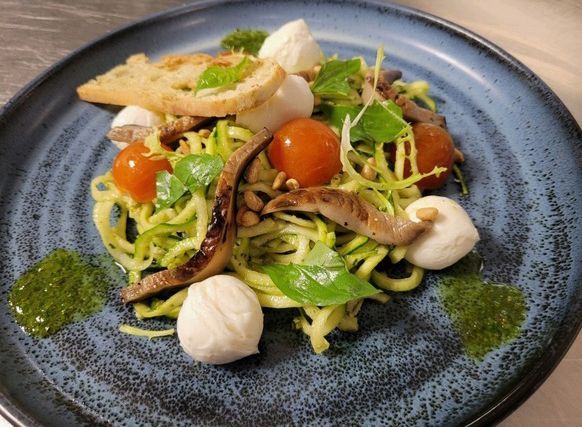 Plated vegetable pasta salad with cherry tomatoes, greens, mushrooms, and basil pesto on a blue plate