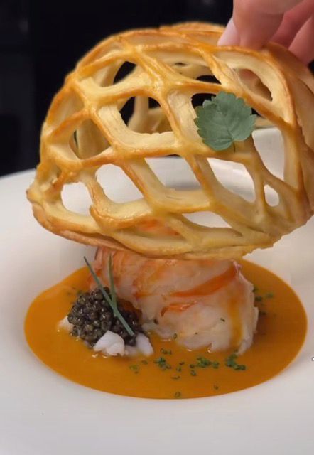 Pastry lattice dome over a plated savory dish with orange sauce and garnish