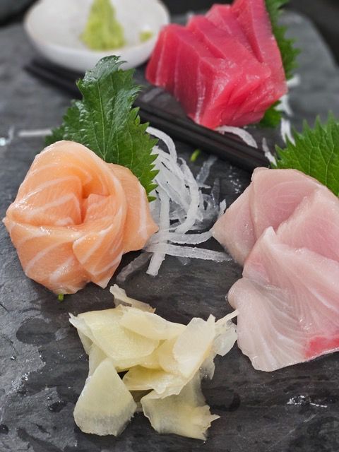 Assorted sashimi on a black stone plate with chopsticks and shredded daikon garnish