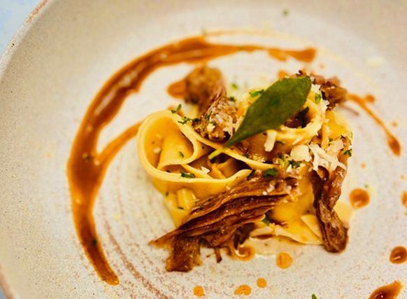 Plated pasta with brown sauce, herbs, and a green leaf garnish on a white dish