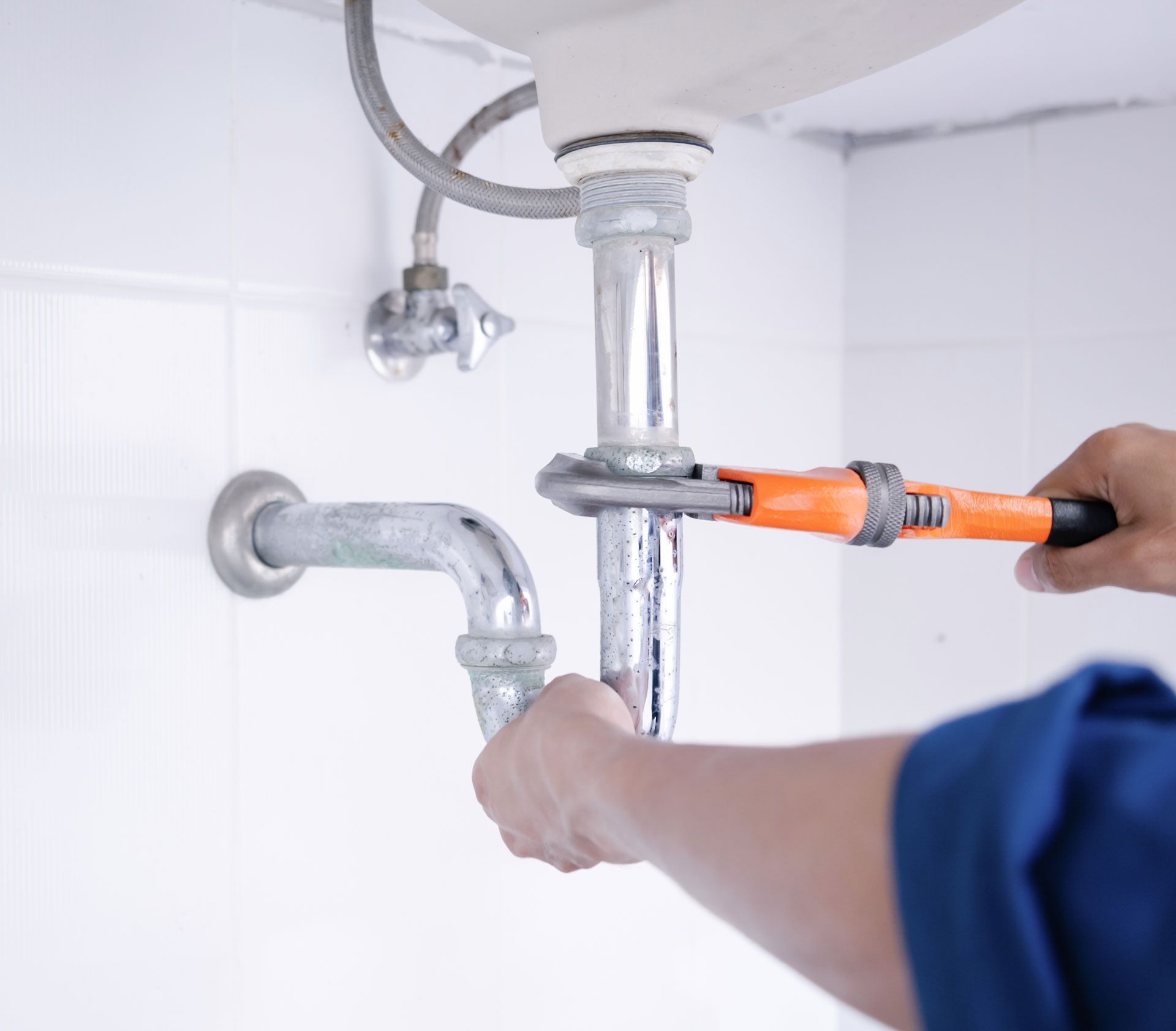 A plumber is fixing a sink pipe with a wrench.