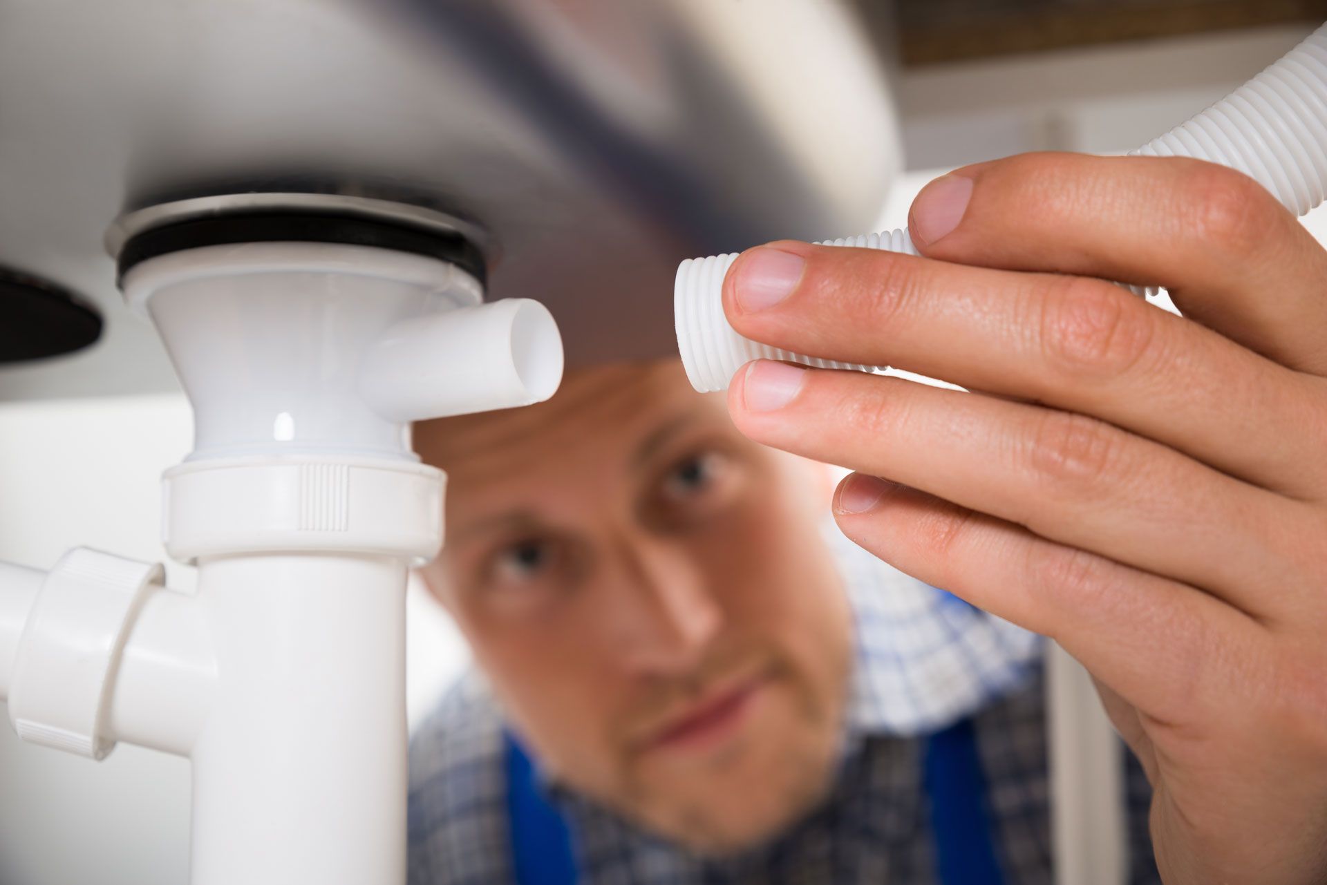 A man is fixing a sink pipe under a sink.