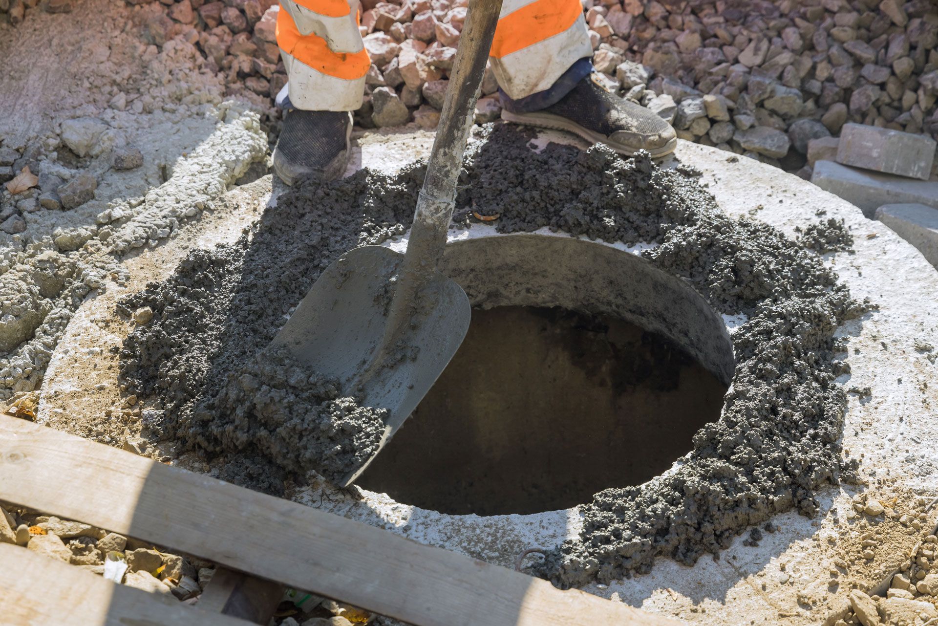 Person in work clothes using a shovel to move wet concrete on a construction site.
