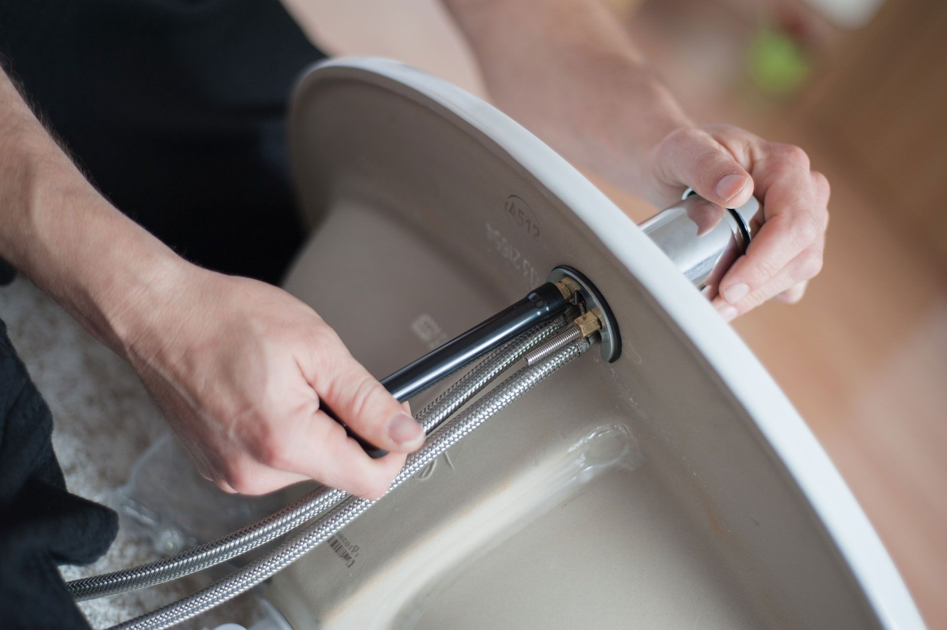 Person installing a faucet in a white sink; hands holding a wrench, chrome faucet.