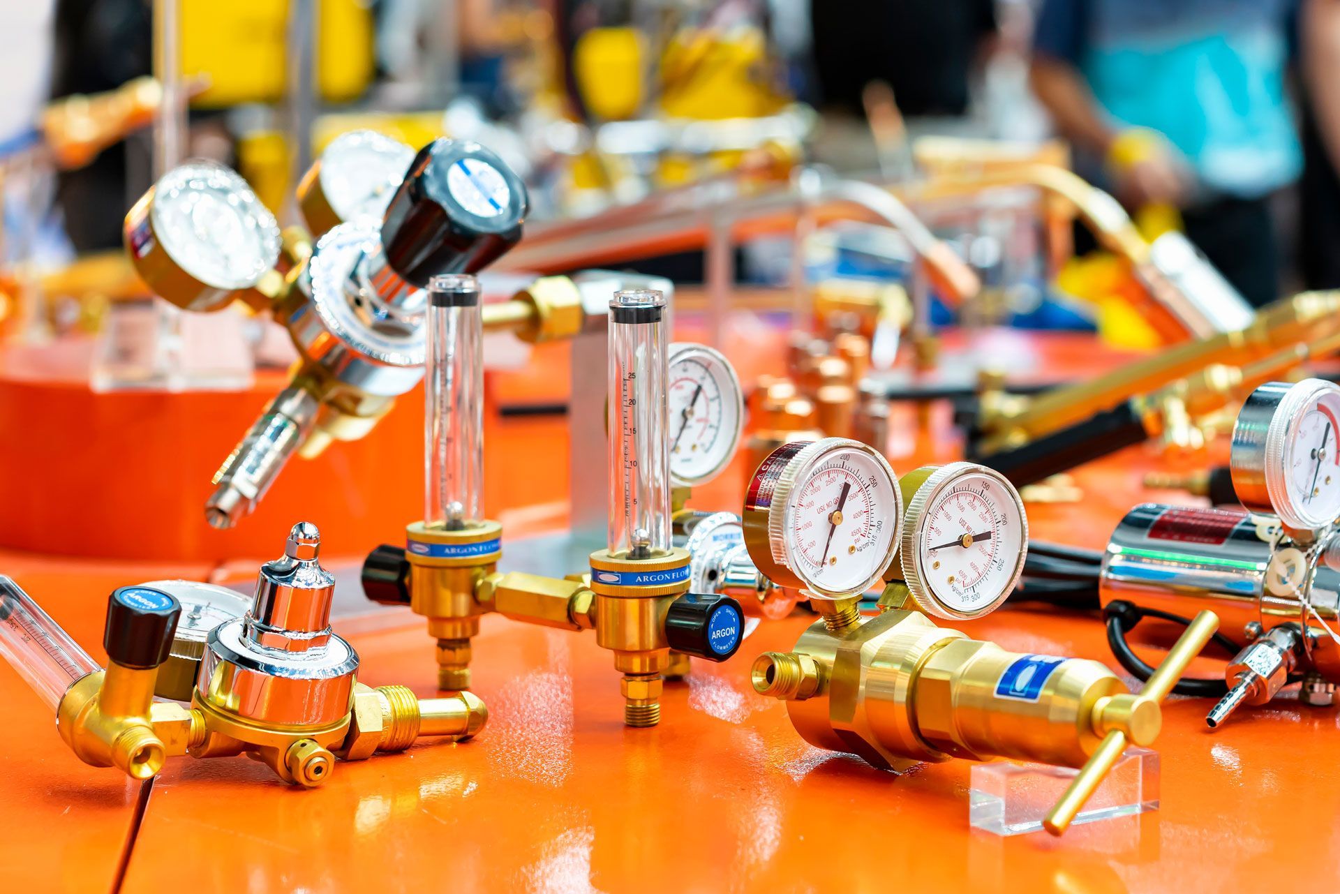 Close-up of multiple gas regulators with gauges and flowmeters displayed on an orange table.