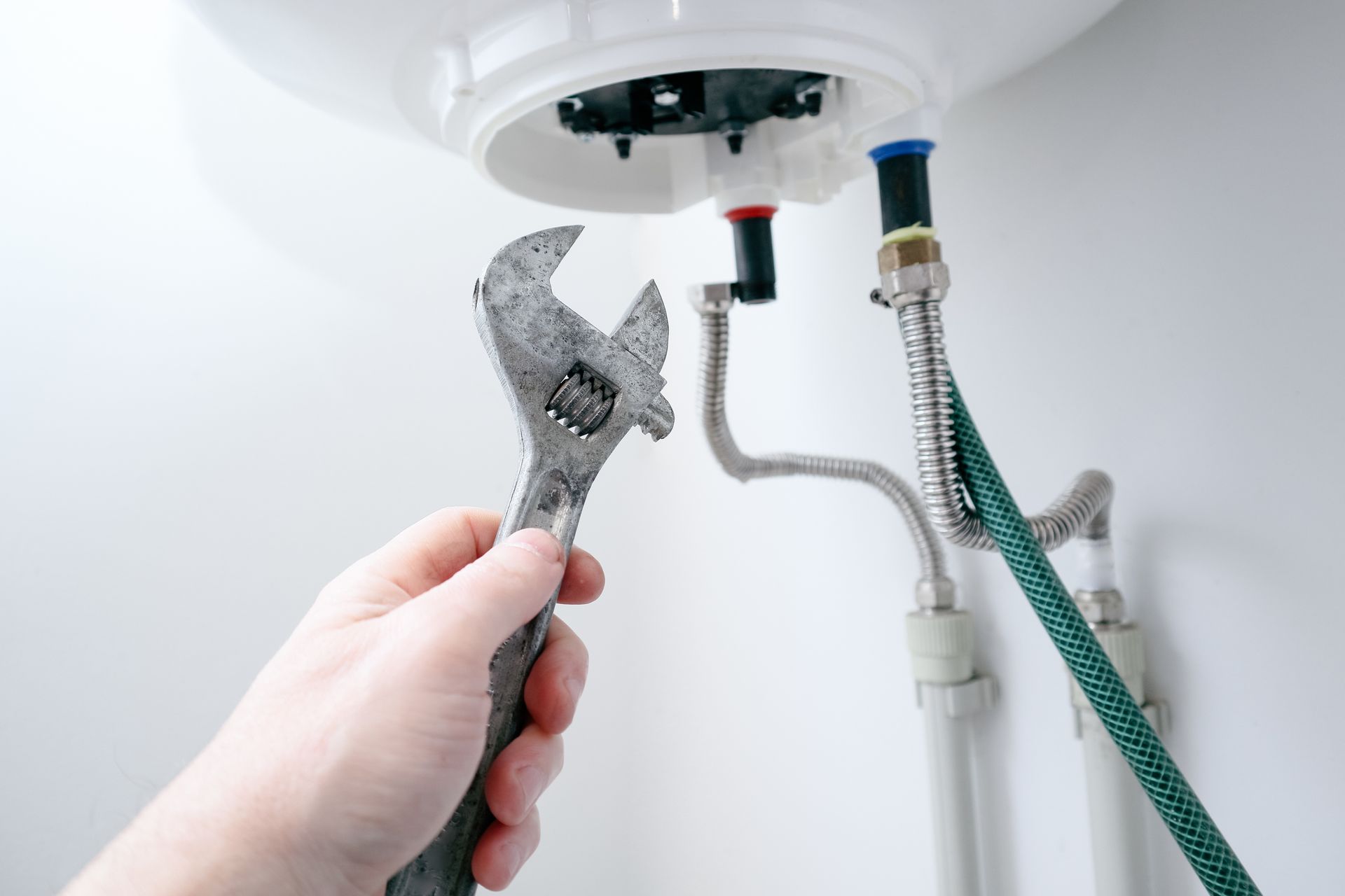 Hand holding wrench, working on plumbing pipes connected to a water heater.