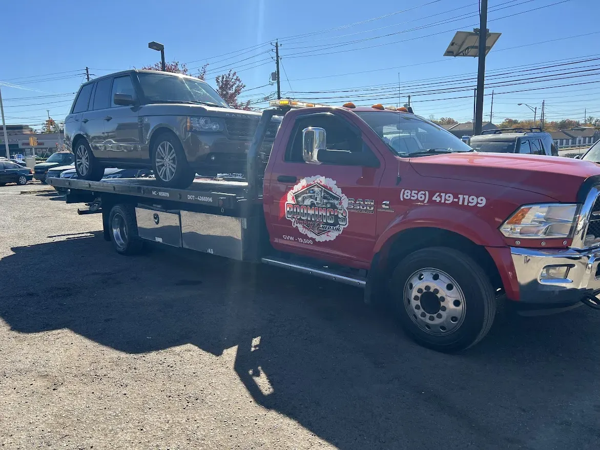 A red tow truck with a silver SUV on its flatbed, parked on asphalt; sunny day.