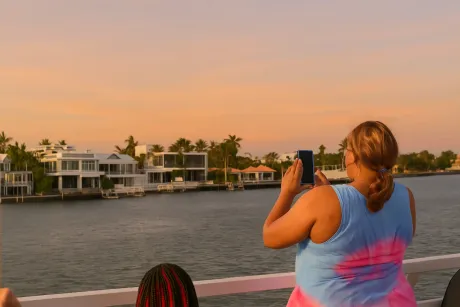 Guest taking photos during a Miami Sunset Cruise while passing waterfront homes.
