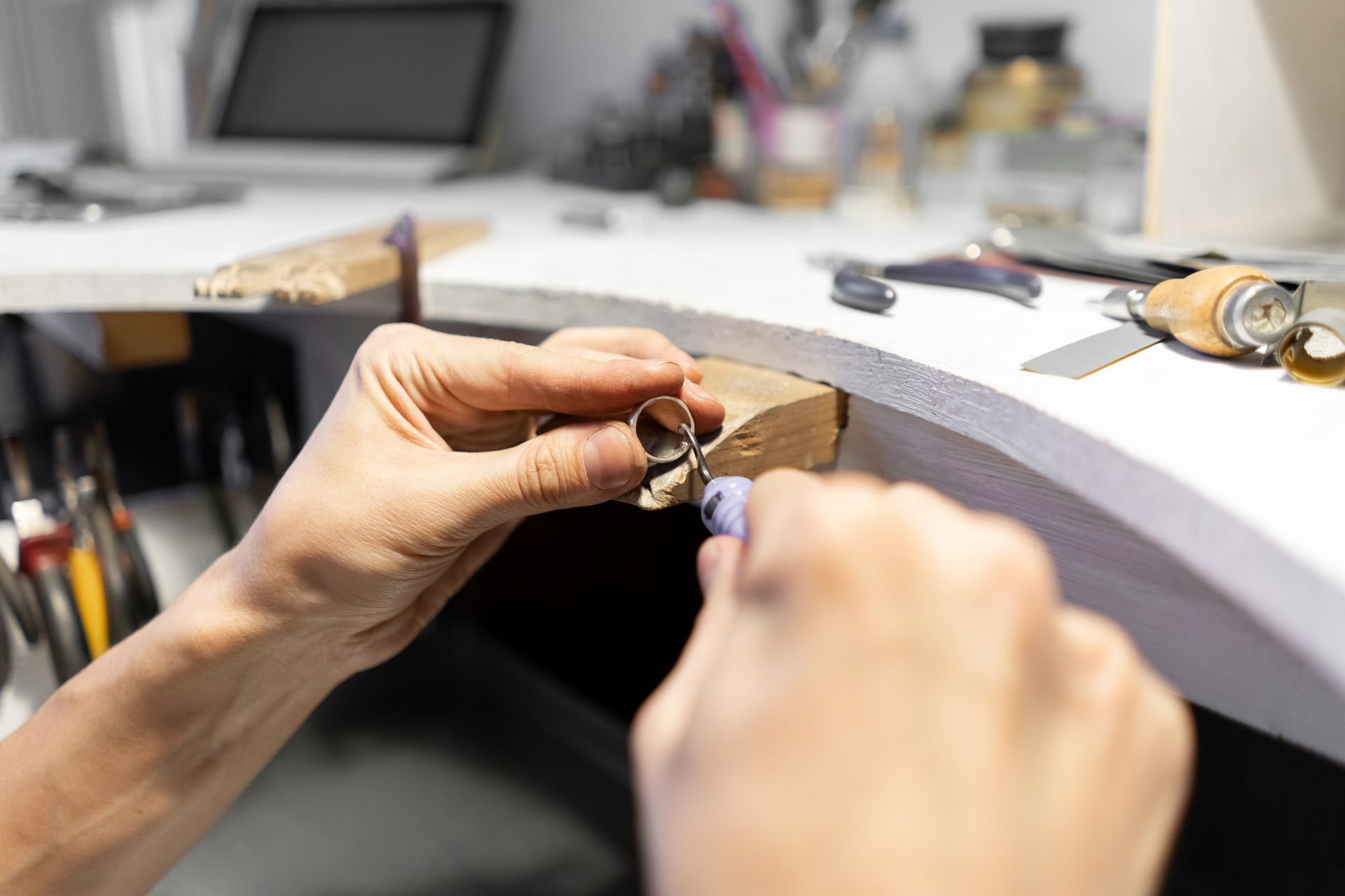 Hände, die an einer Werkbank in einer Werkstatt an einem kleinen Schmuckstück arbeiten