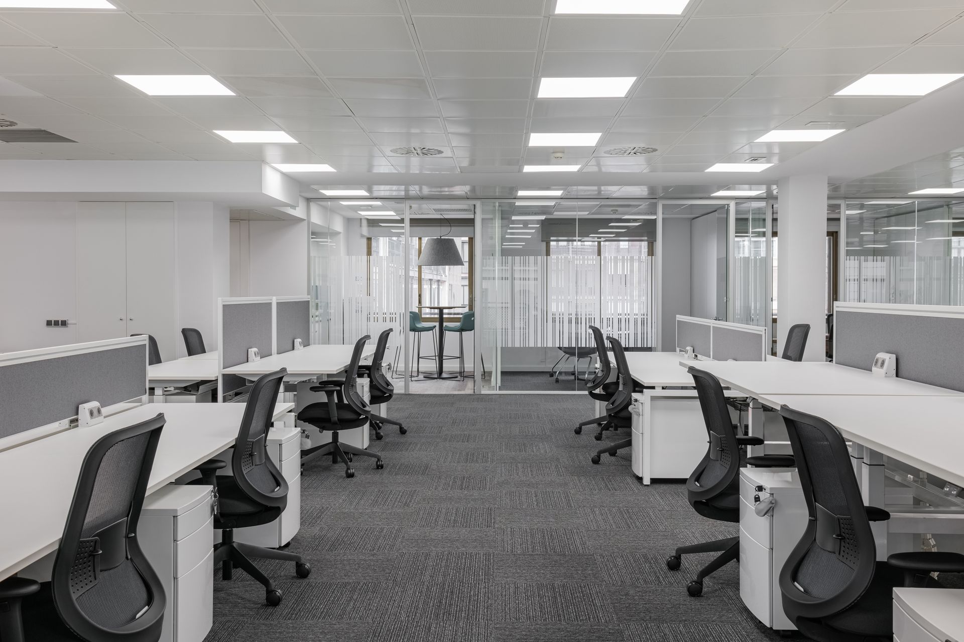 Ein leeres, modernes Büro mit Reihen von Schreibtischen, schwarzen Stühlen und Besprechungsräumen mit Glaswänden.