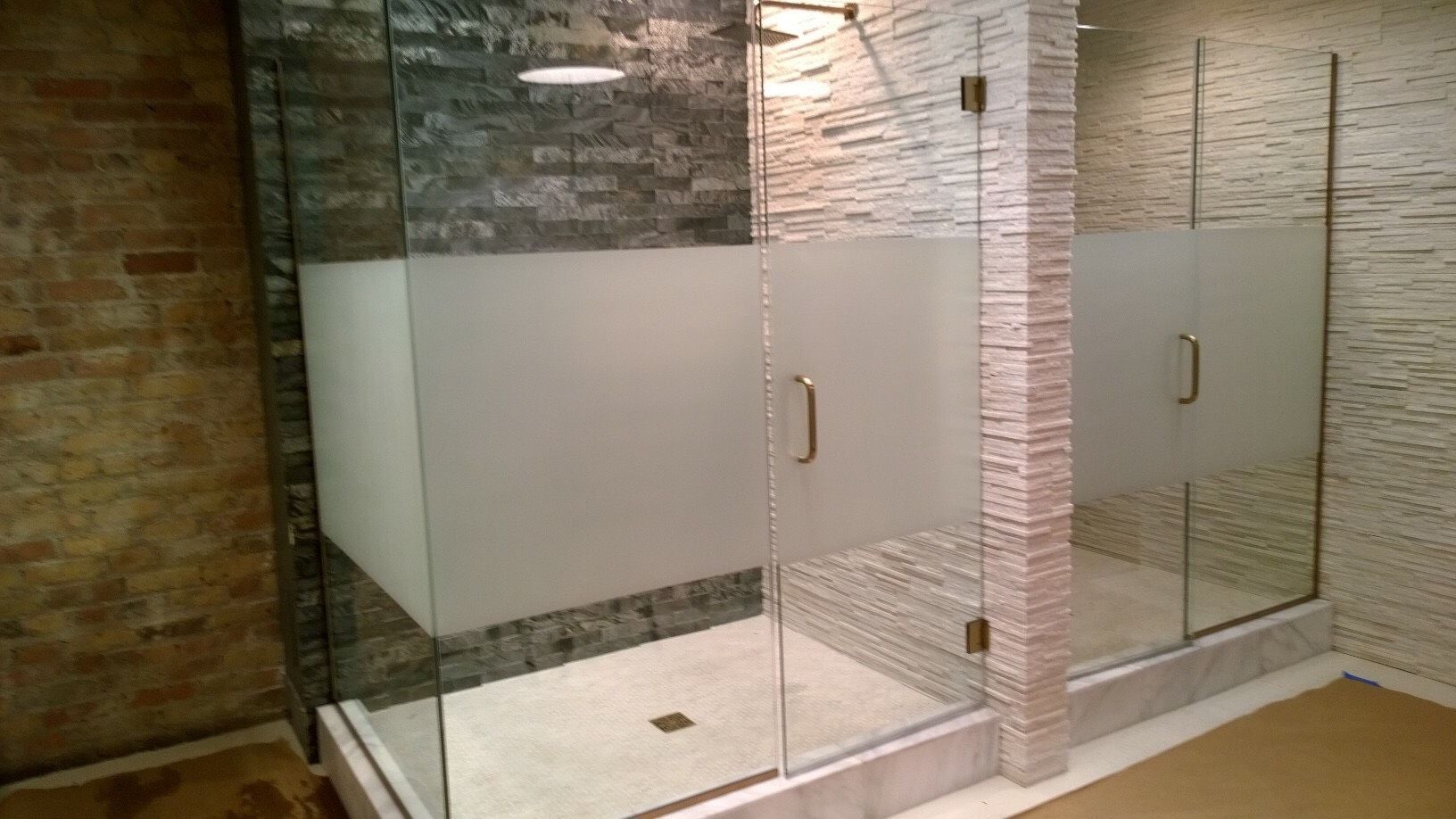 A bathroom with a glass shower door and a brick wall.