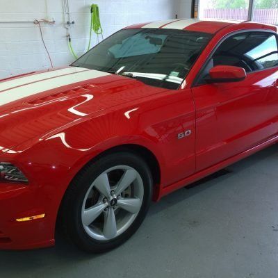 A red mustang with white stripes is parked in a garage