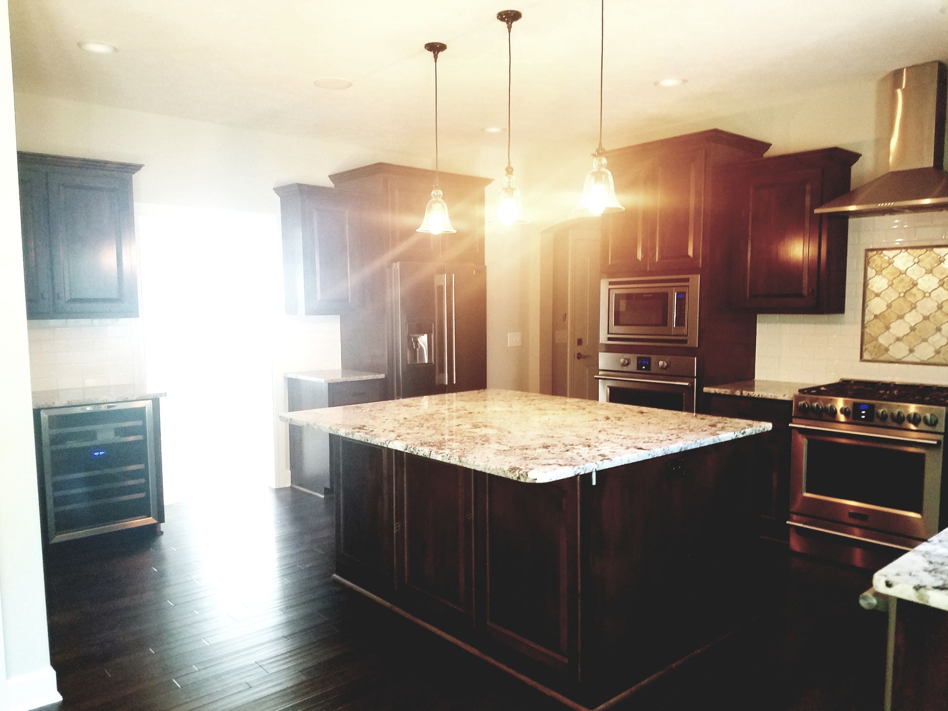 A spacious kitchen featuring dark wood cabinets, a large granite-topped island, stainless steel appliances, and wood floors.