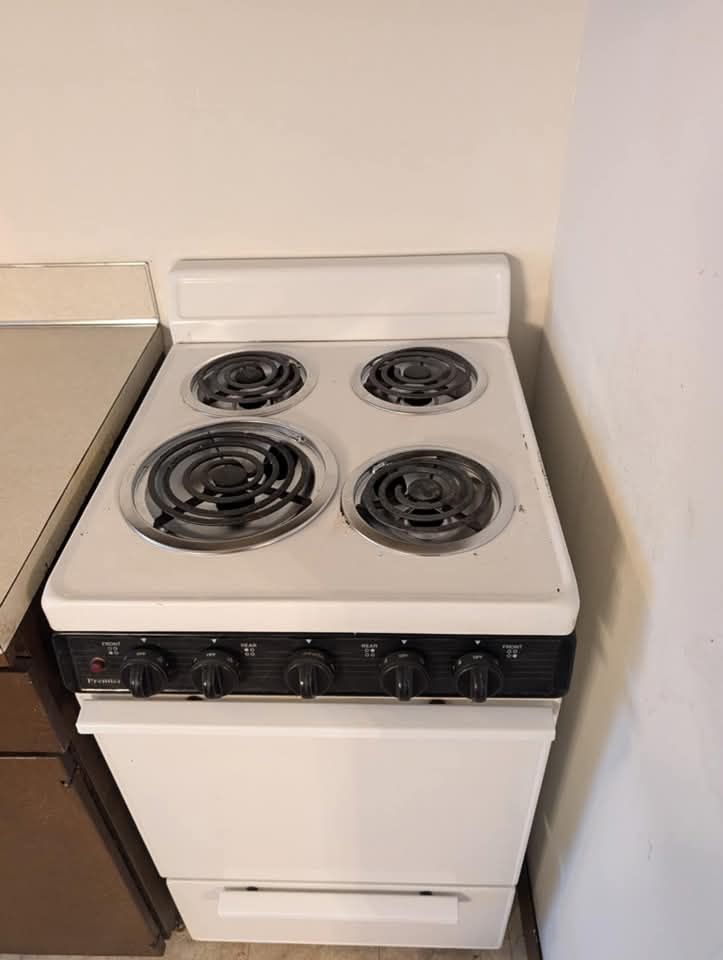 A white, four-burner electric stove sits in a kitchen next to a brown cabinet and a white wall.