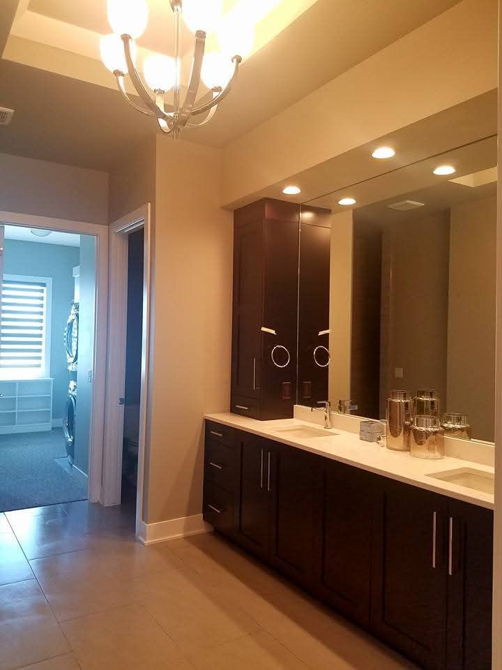 A modern bathroom vanity with dark wood cabinets, white countertops, and a large mirror under recessed lighting.