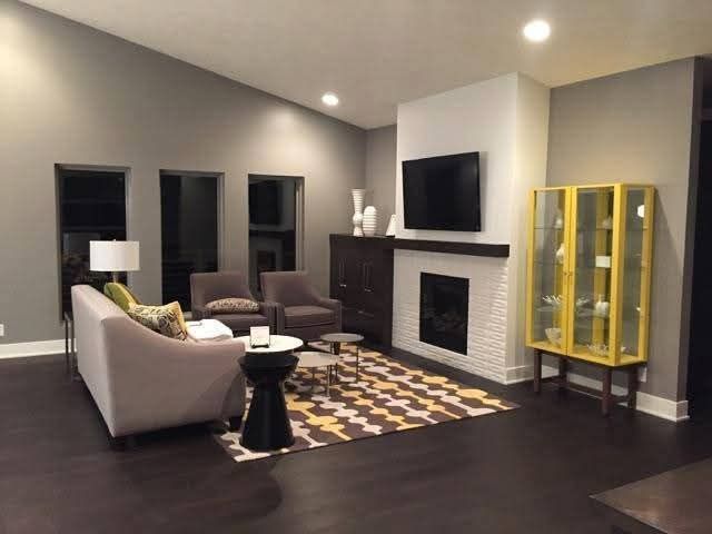 A modern living room with a grey sofa, patterned rug, fireplace, TV, and a yellow display cabinet on dark wood floors.