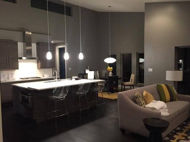 A modern open-concept kitchen and living area with a grey color palette, kitchen island, and contemporary lighting.