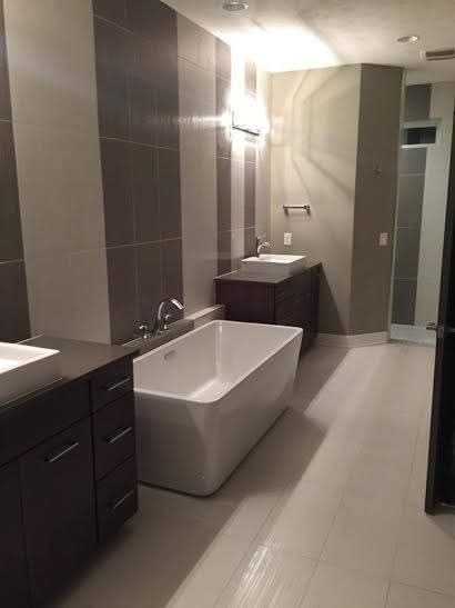 A modern bathroom featuring a white freestanding bathtub between two dark brown vanity cabinets with white sinks.