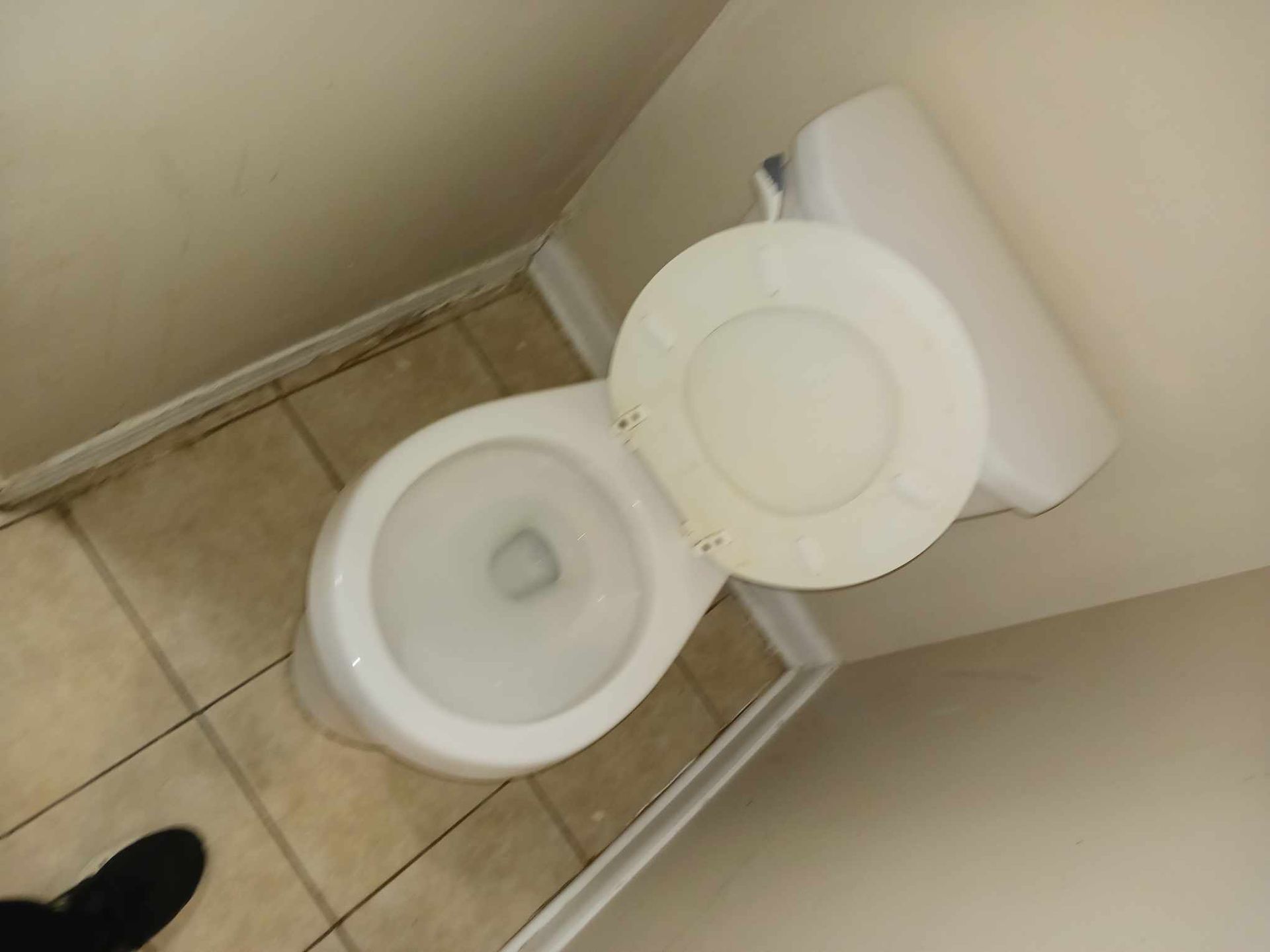 An overhead view of a white porcelain toilet with the lid and seat in an upright, open position in a tiled bathroom.