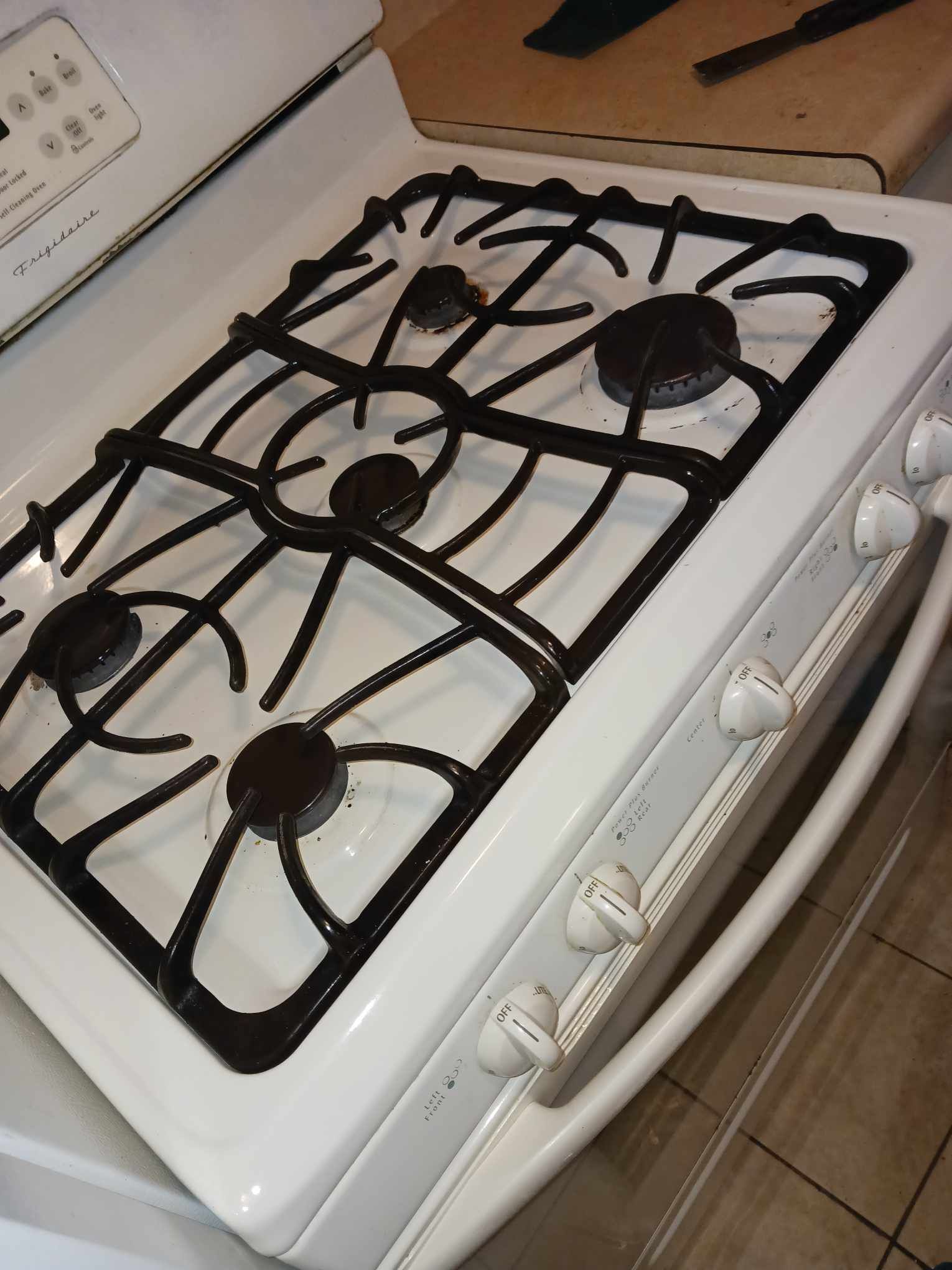 A white gas range stove featuring a black grate with four burners and a control panel with knobs on the front.