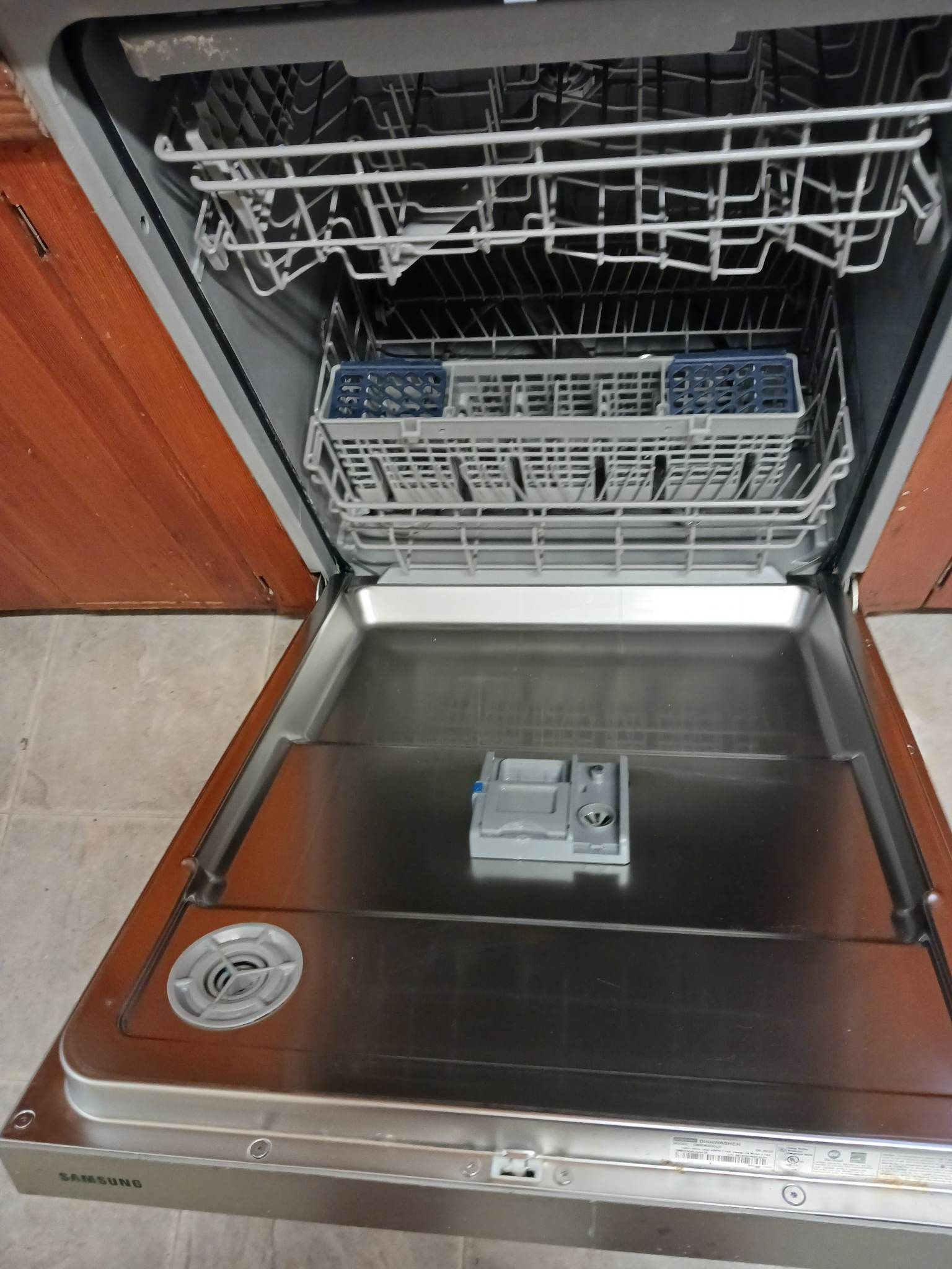 Open stainless steel interior of a dishwasher with two empty wire racks and a detergent dispenser on the door.