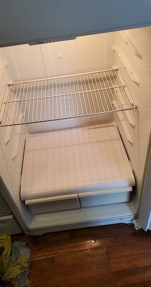 The interior of a clean, empty white refrigerator with one wire shelf and two bottom crisper drawers.