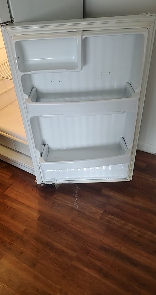 The inside of a white refrigerator door with three empty storage bins, resting on a wooden floor.