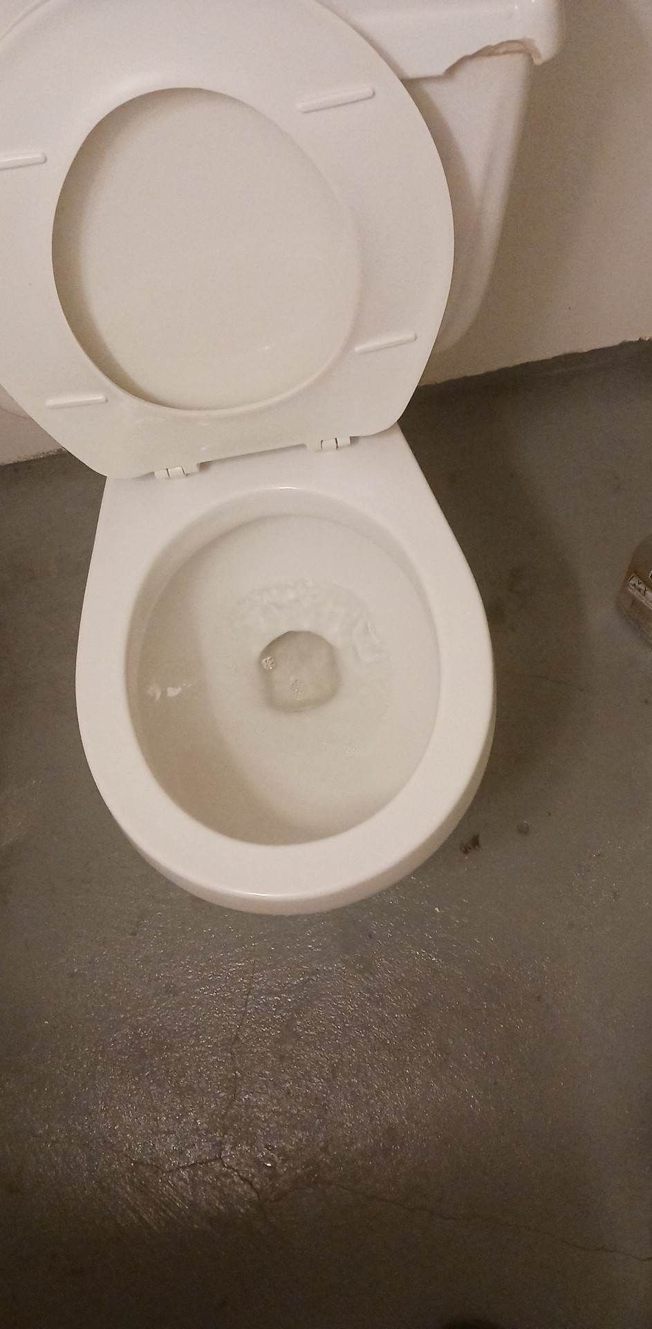 A top-down view of a white porcelain toilet with the lid and seat raised, situated on a gray tiled floor.