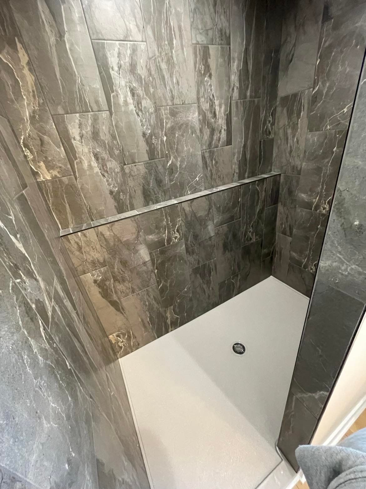 A walk-in shower with dark brown stone-patterned tile walls and a white rectangular shower floor base.