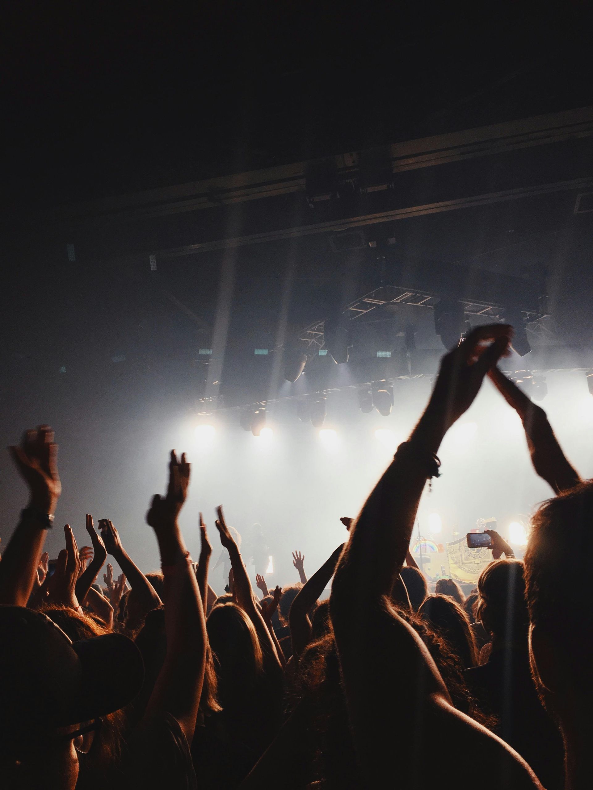 Concert crowd with arms raised towards a brightly lit stage. Silhouettes of people enjoying the music.