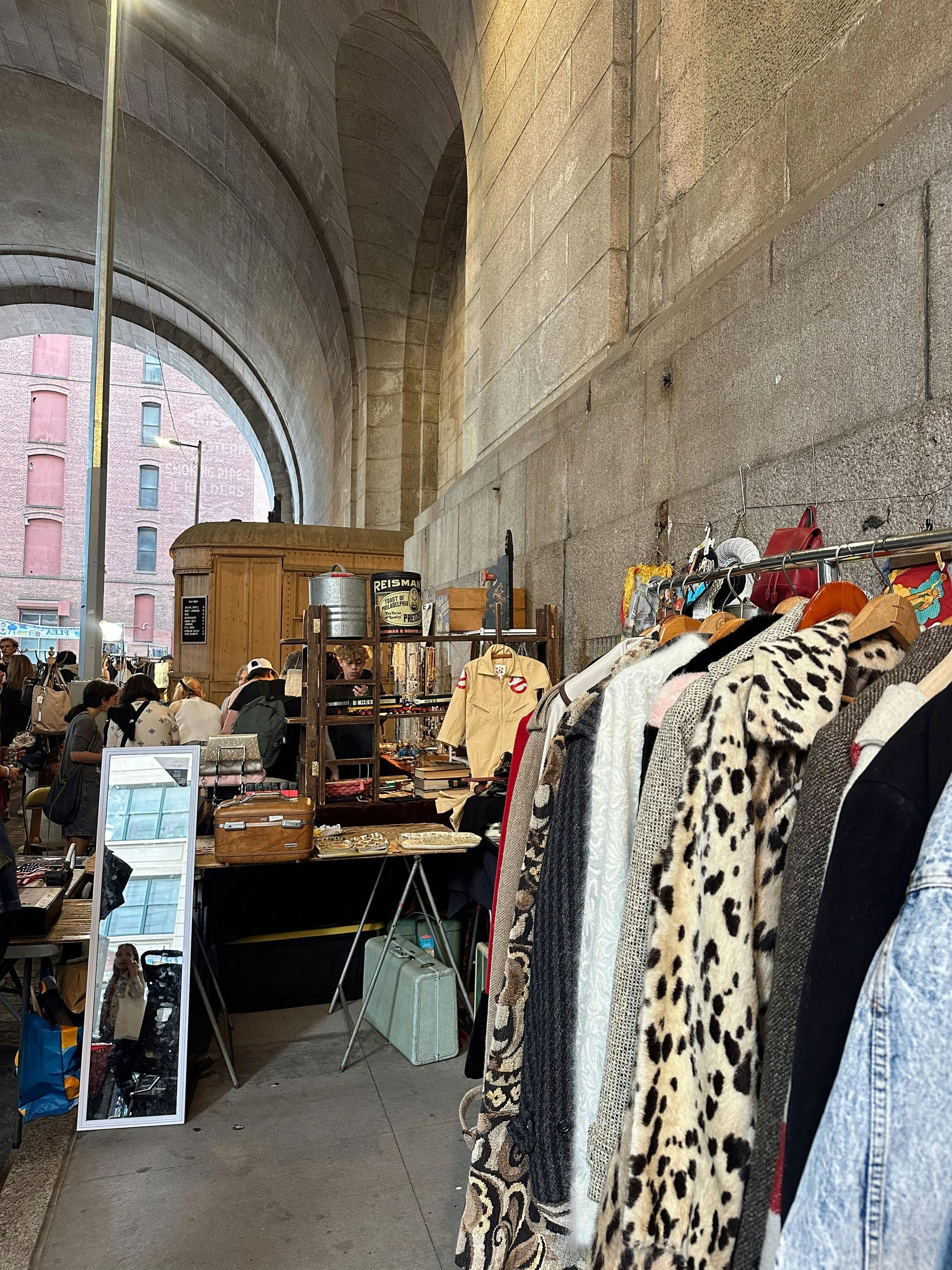 Clothes racks and vendor tables at an outdoor market under a brick archway.