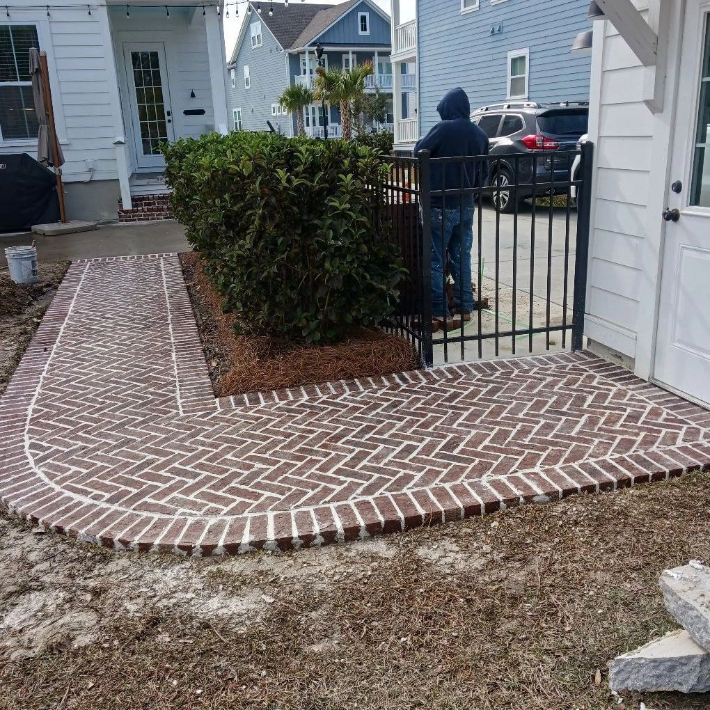 Brick walkway and ramp beside a house entrance, with a person standing by a black gate.