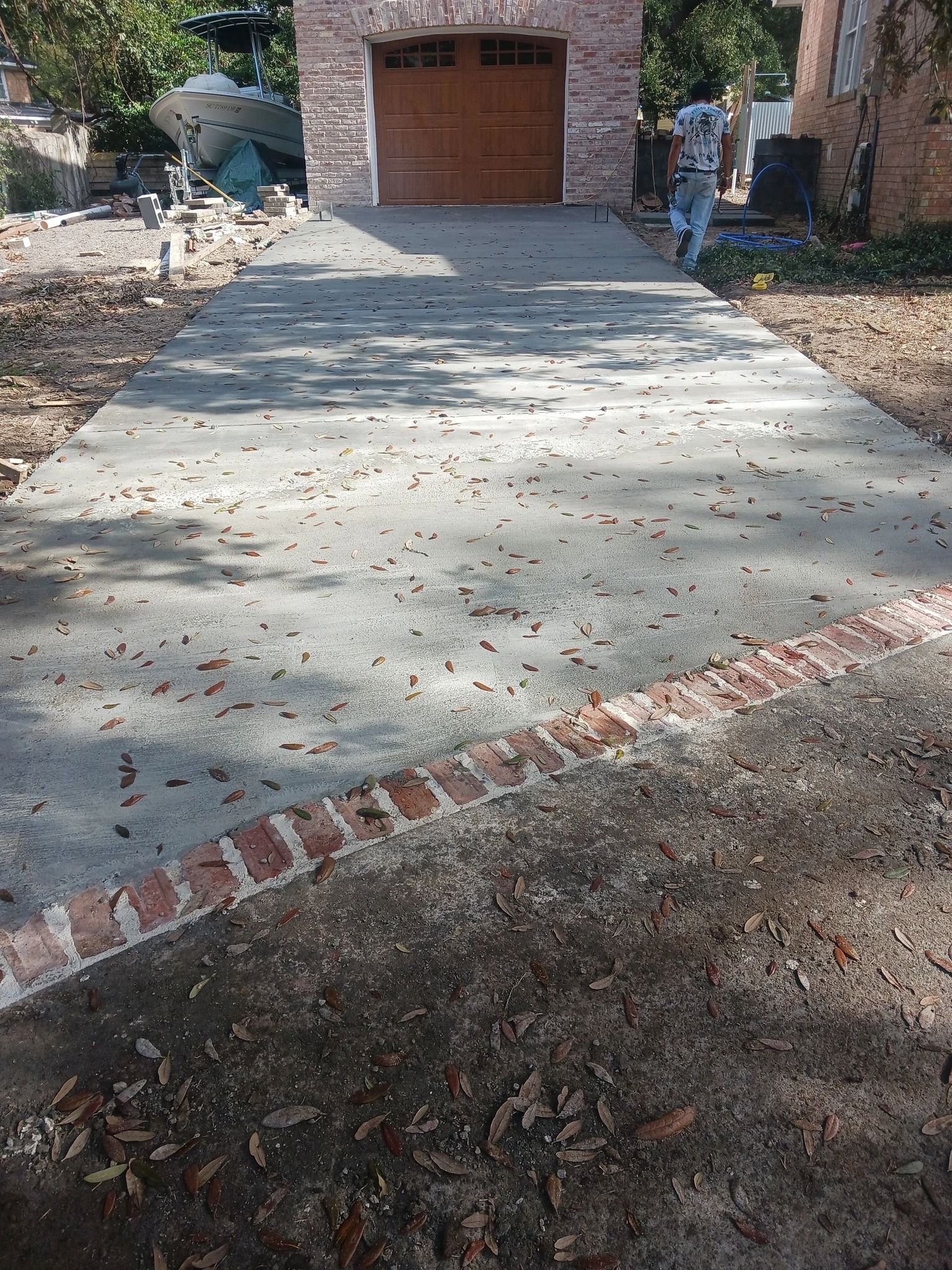Concrete driveway leading to a wooden garage door, with a brick edge and leaves scattered on both sides