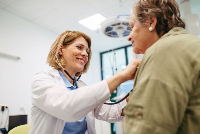 Doctor using a stethoscope to examine a patient's chest in a medical office.