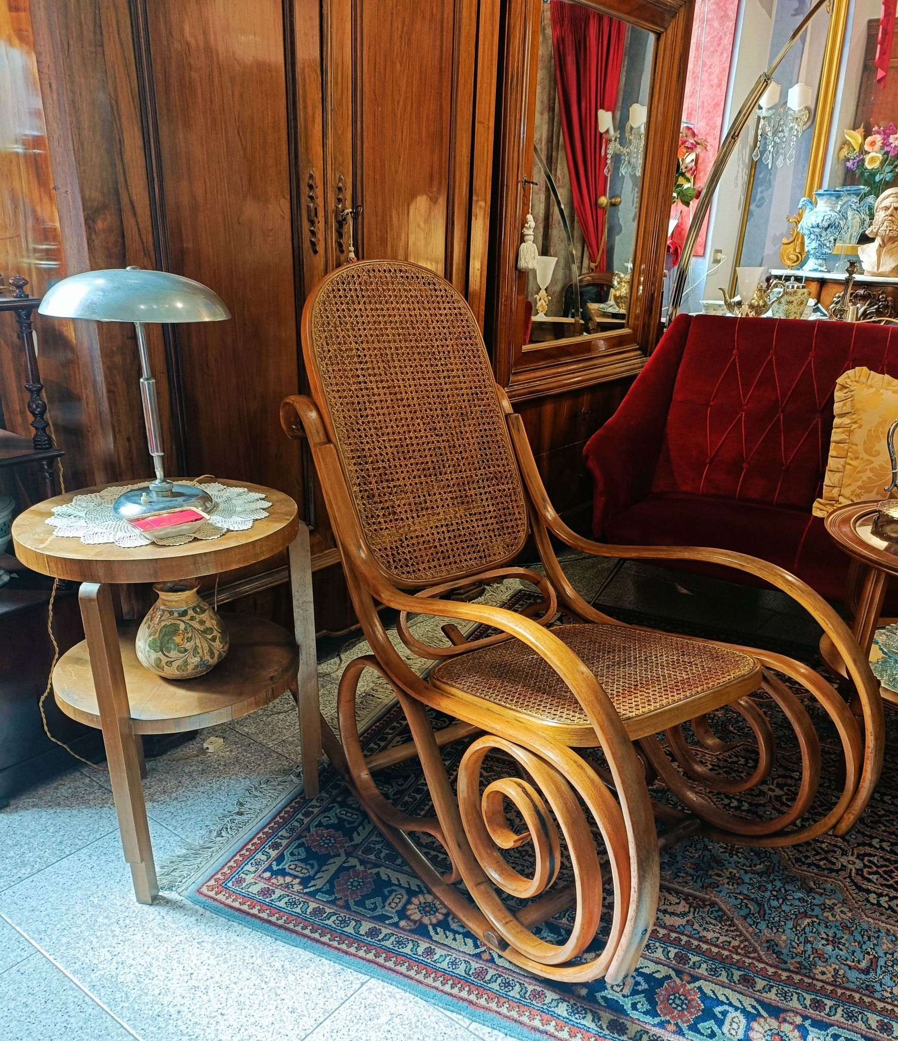 Una sedia a dondolo di legno è posizionata in una stanza accanto a un tavolo e una lampada.