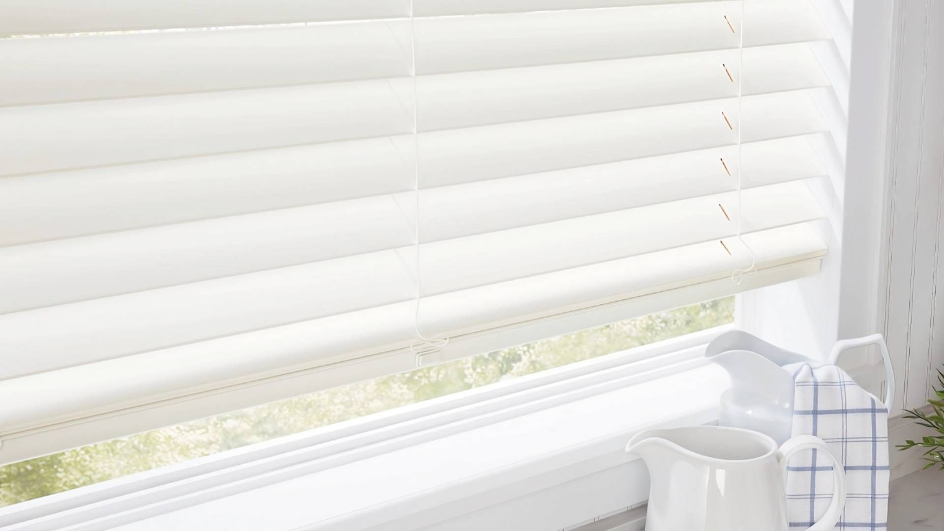 Cream-colored Hunter Douglas Parkland® Wood Blinds on a kitchen window with two pitchers on the coun