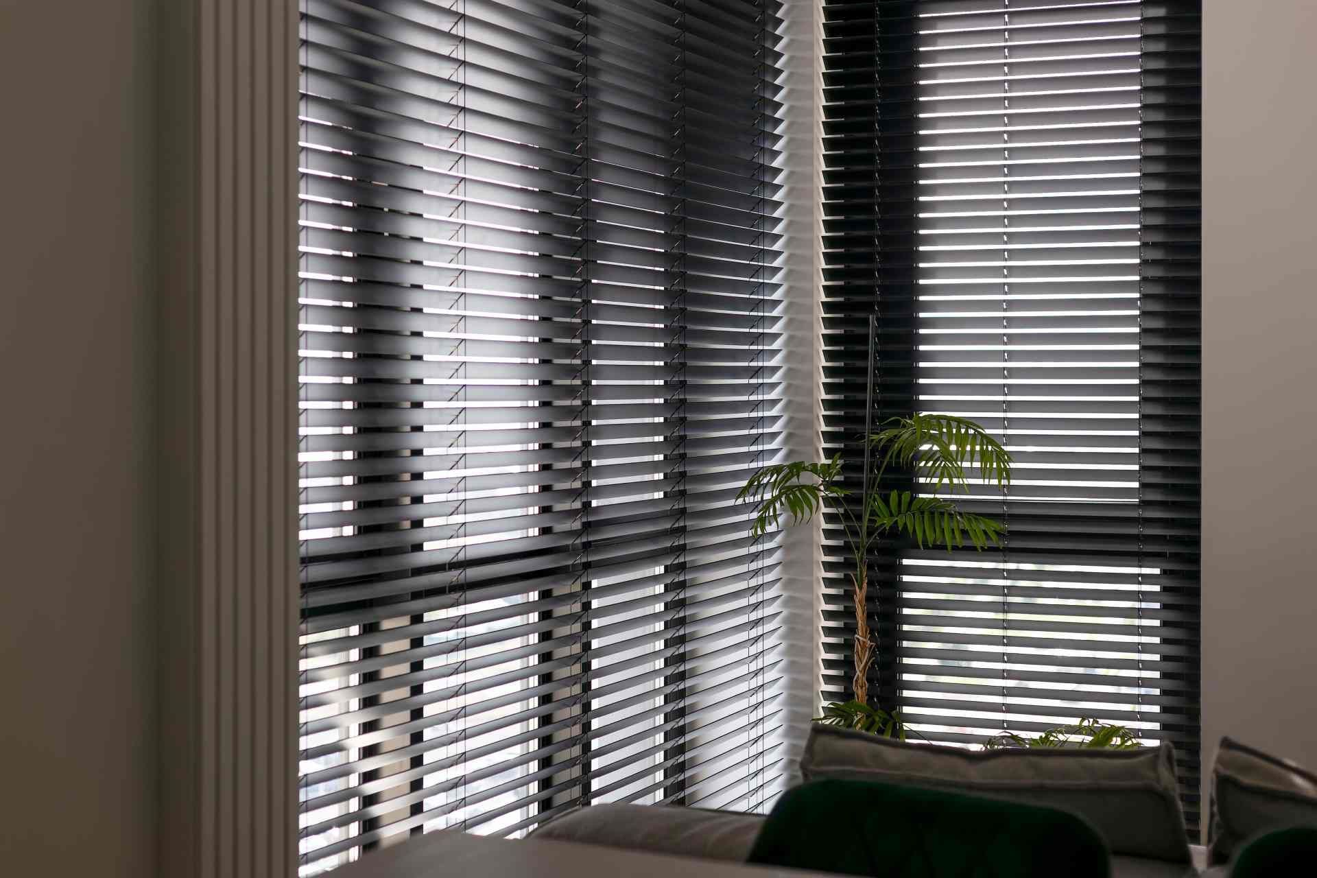 Window treatments for corner windows in a dimly lit interior space with a small house plant  at Adva