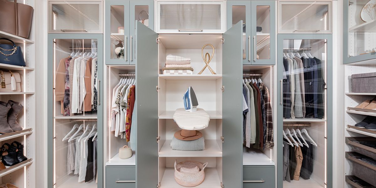 A arctic and spruce color finish walk in closet filled with lots of clothes and shoes.