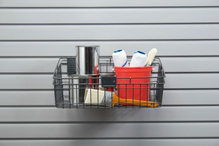 A wire basket filled with cleaning supplies is hanging on a wall.
