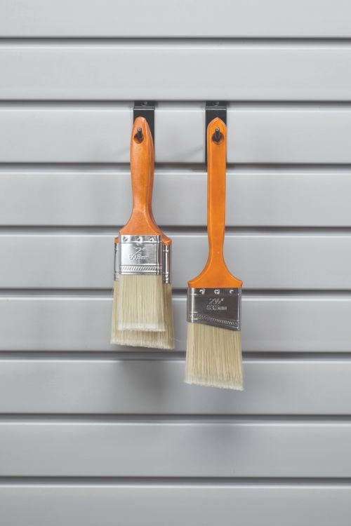 Two paint brushes with orange handles are hanging on a wall.