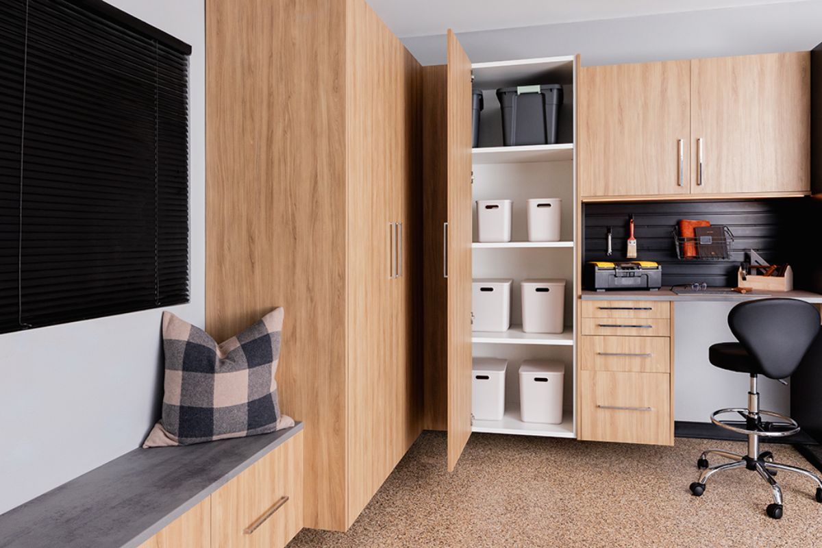 A room with wooden cabinets , a bench , a desk and a chair.