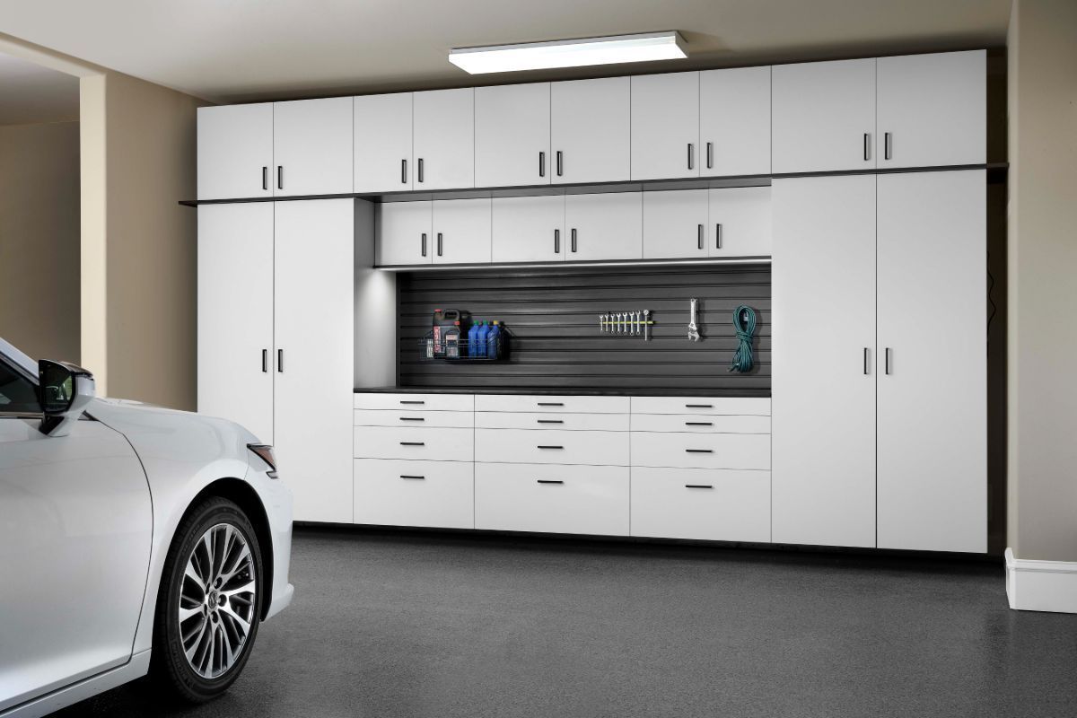 A white car is parked in a garage with white cabinets.