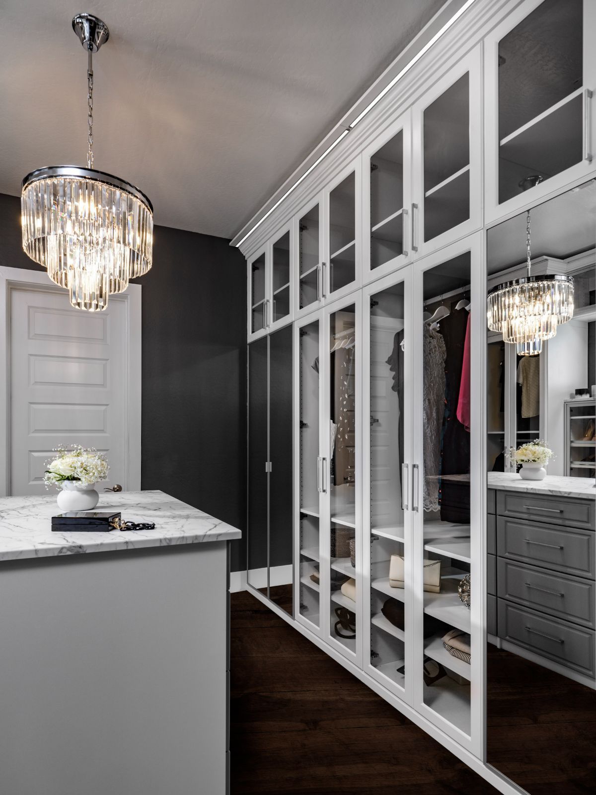 A walk in closet with glass doors and a chandelier hanging from the ceiling.